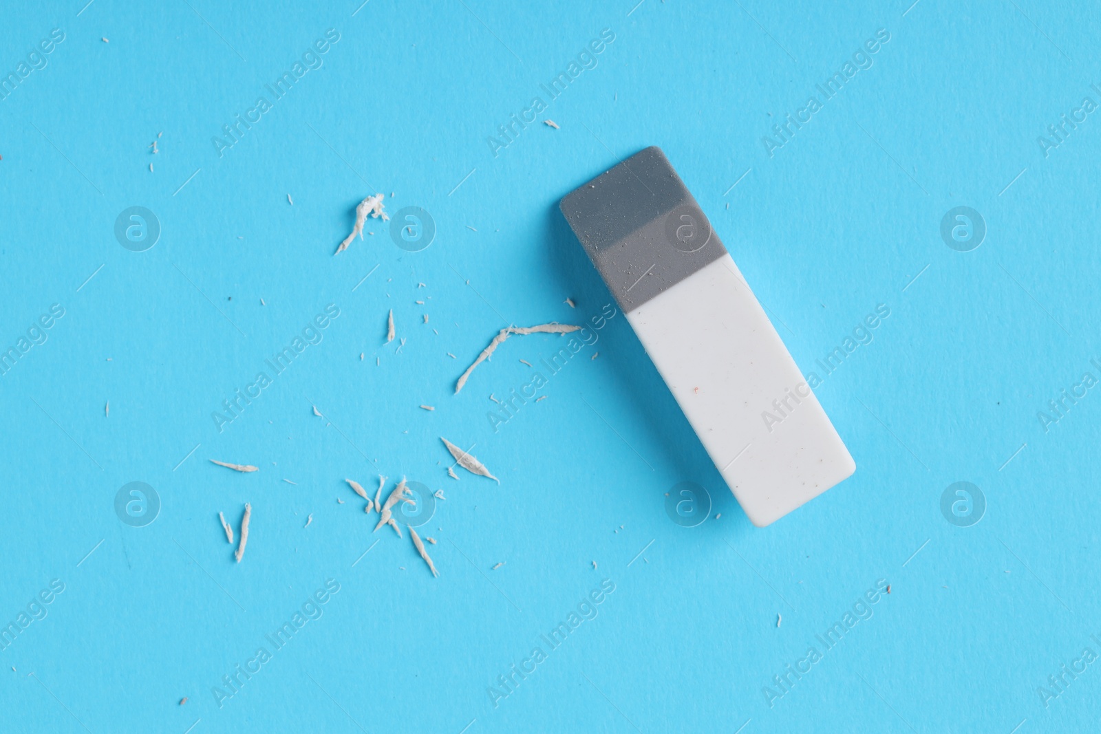 Photo of One eraser and scraps on light blue background, top view