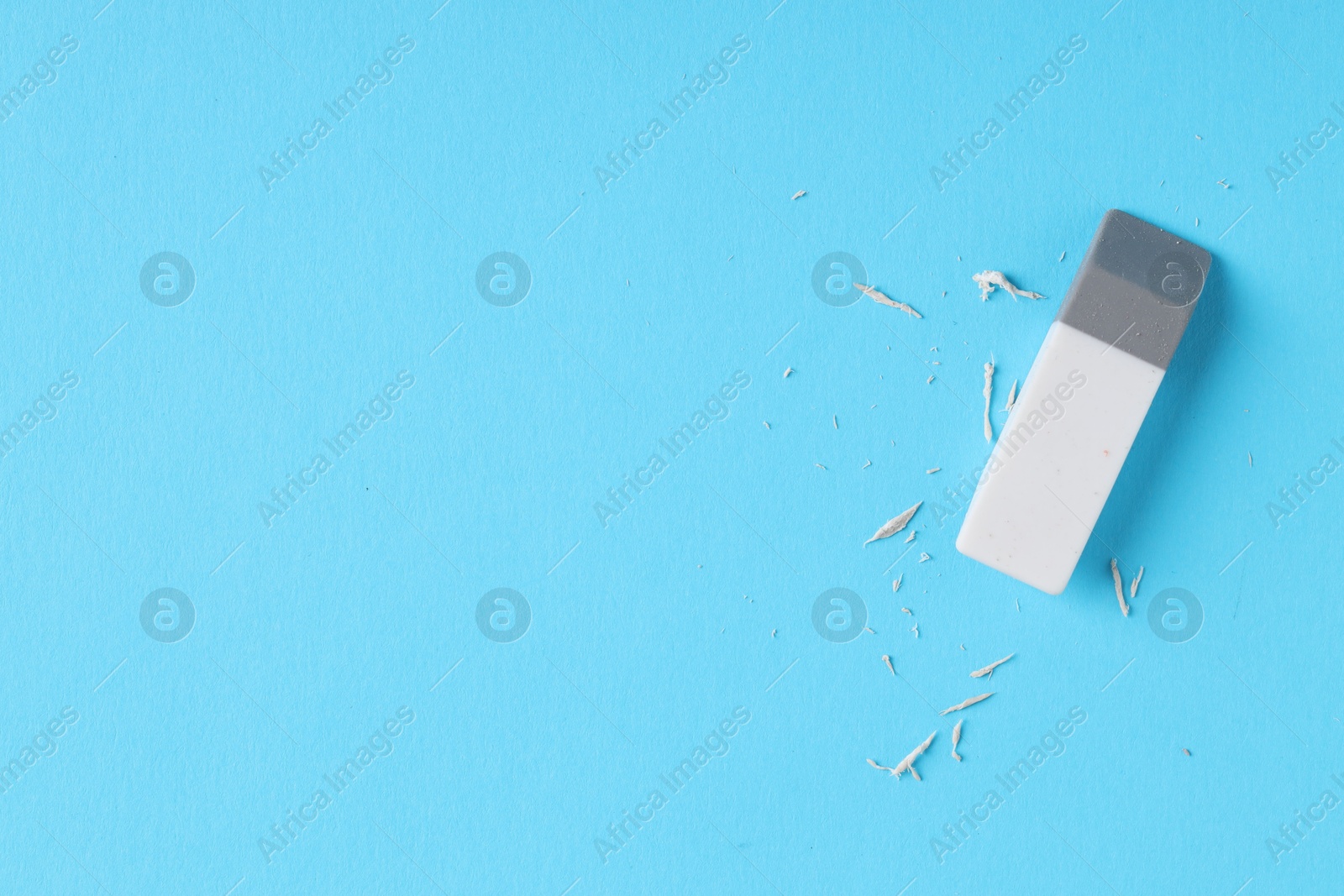 Photo of One eraser and scraps on light blue background, top view. Space for text