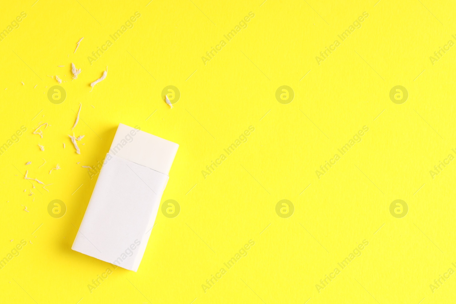 Photo of One eraser and scraps on yellow background, top view. Space for text