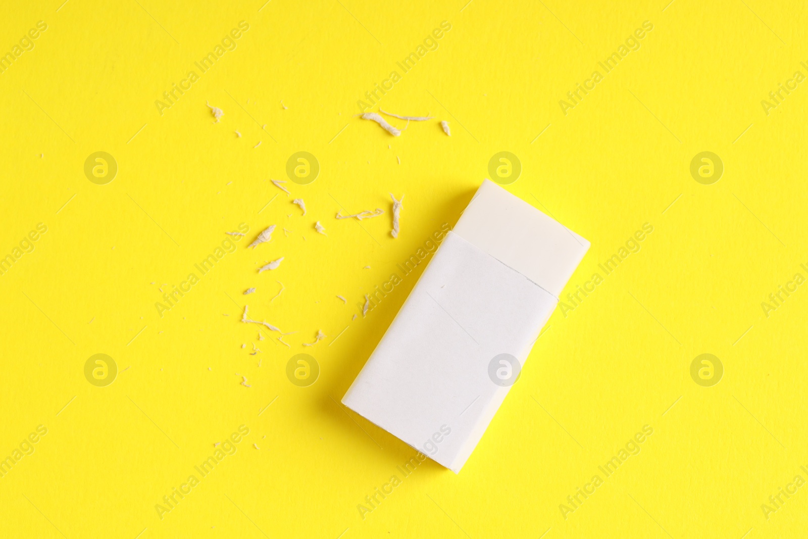 Photo of One eraser and scraps on yellow background, top view