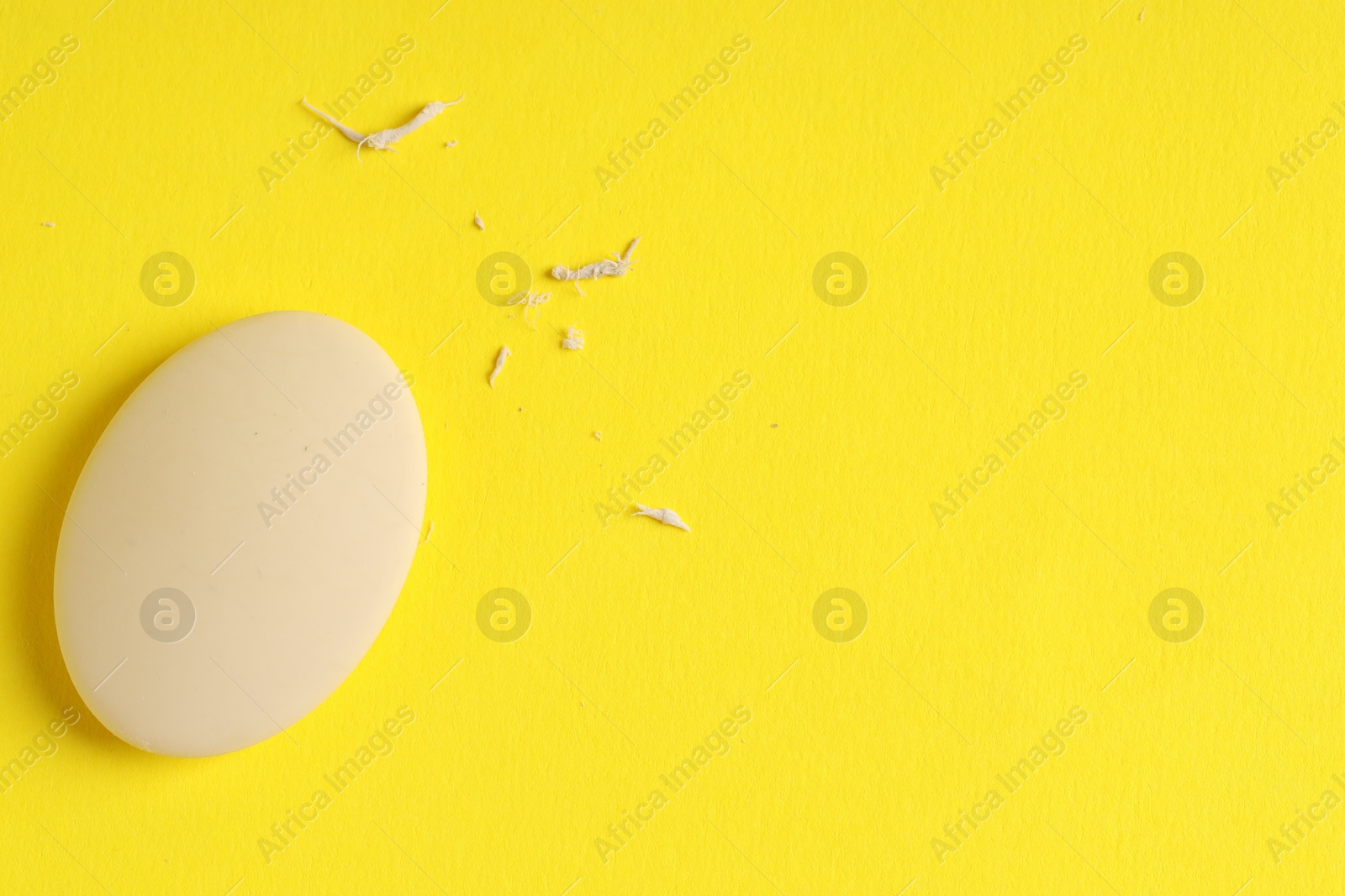 Photo of One eraser and scraps on yellow background, top view. Space for text