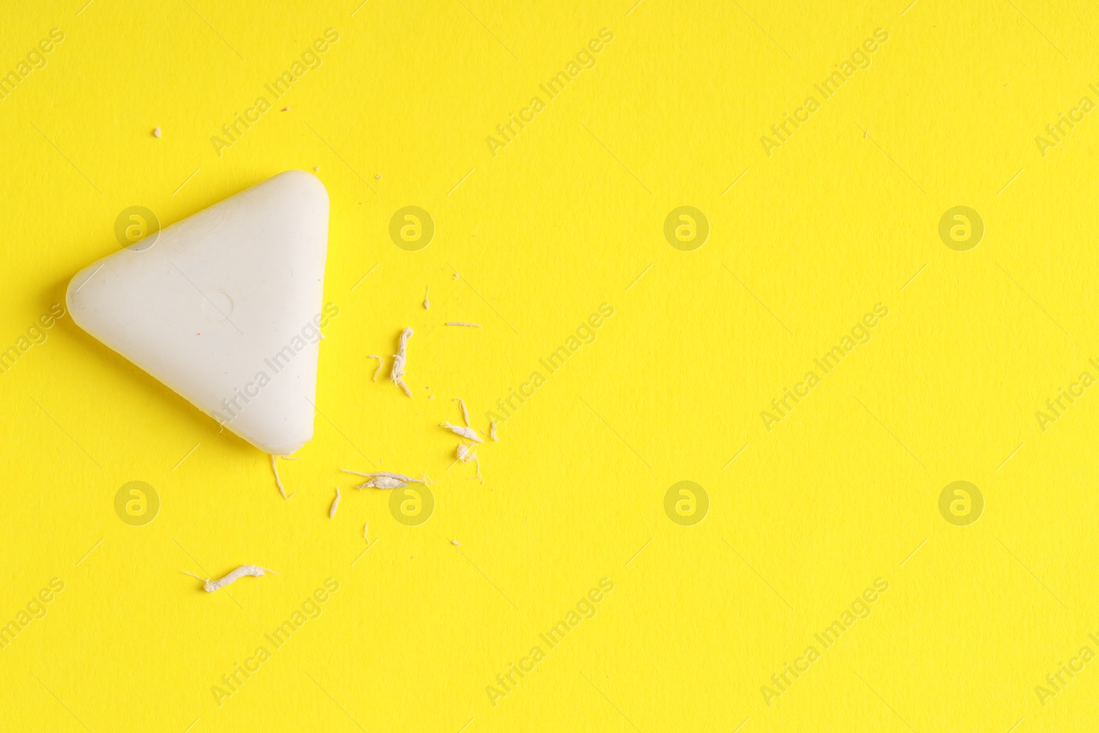 Photo of One eraser and scraps on yellow background, top view. Space for text