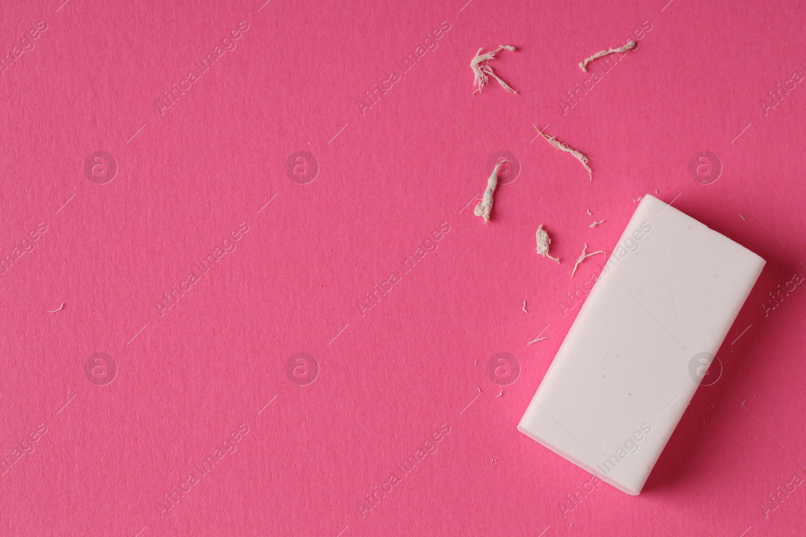 Photo of One eraser and scraps on pink background, top view. Space for text