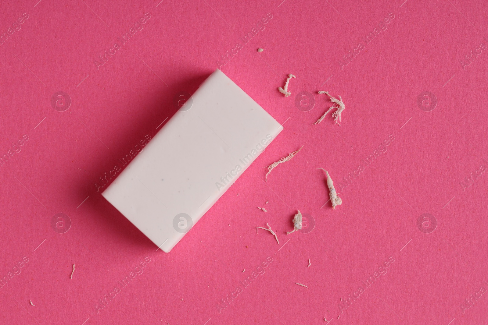 Photo of One eraser and scraps on pink background, top view