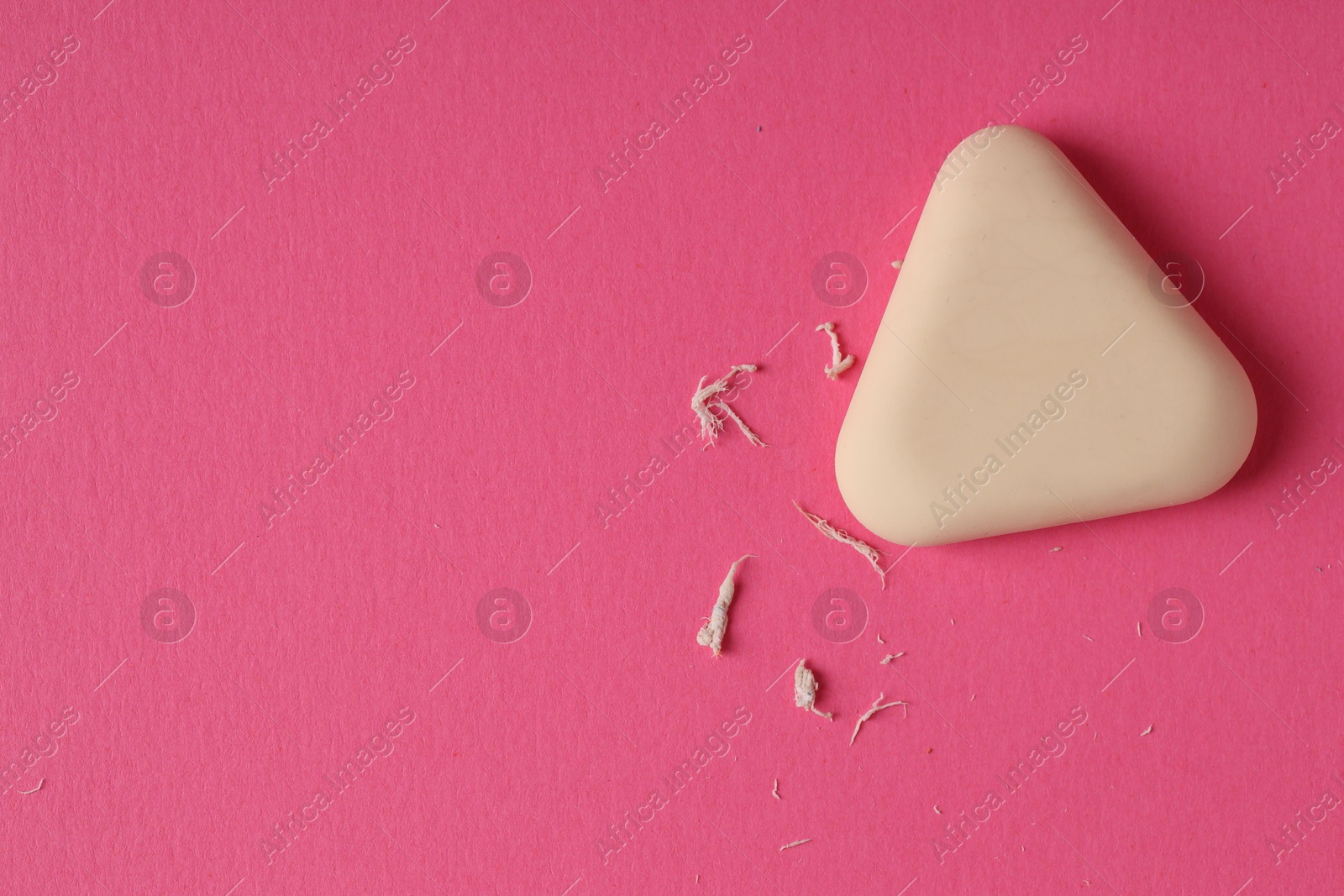 Photo of One eraser and scraps on pink background, top view. Space for text