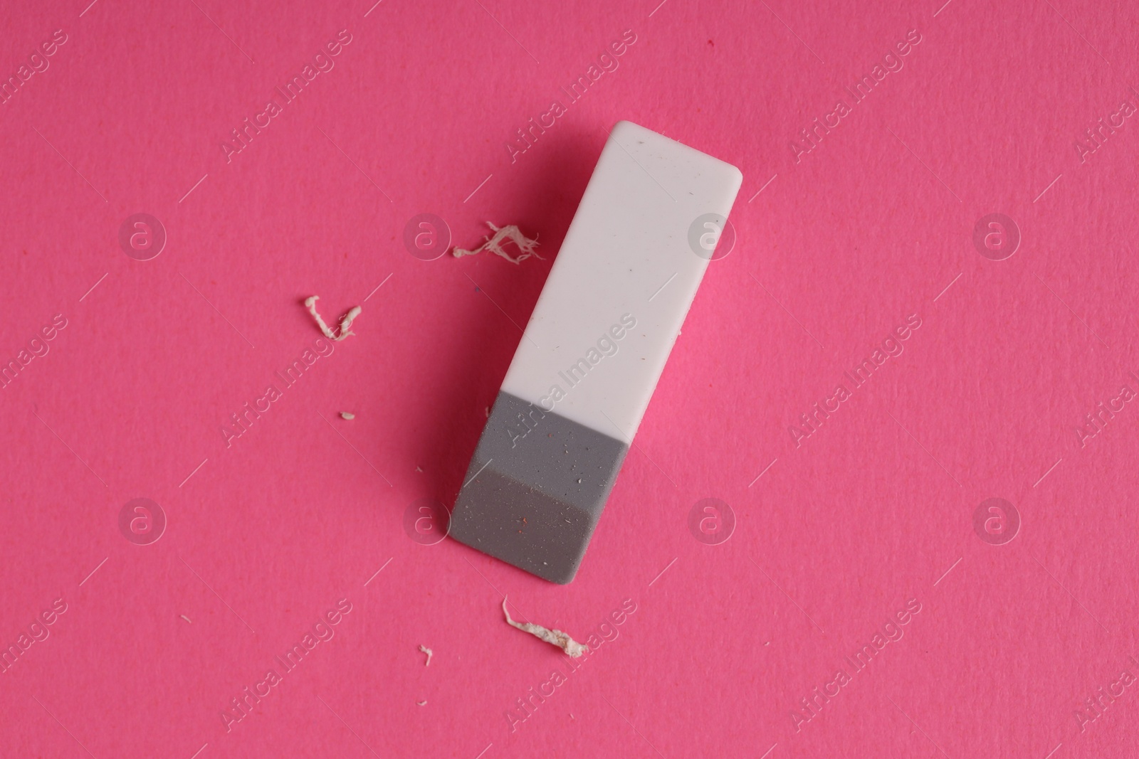 Photo of One eraser and scraps on pink background, top view