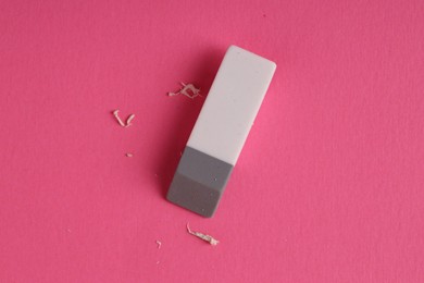 Photo of One eraser and scraps on pink background, top view