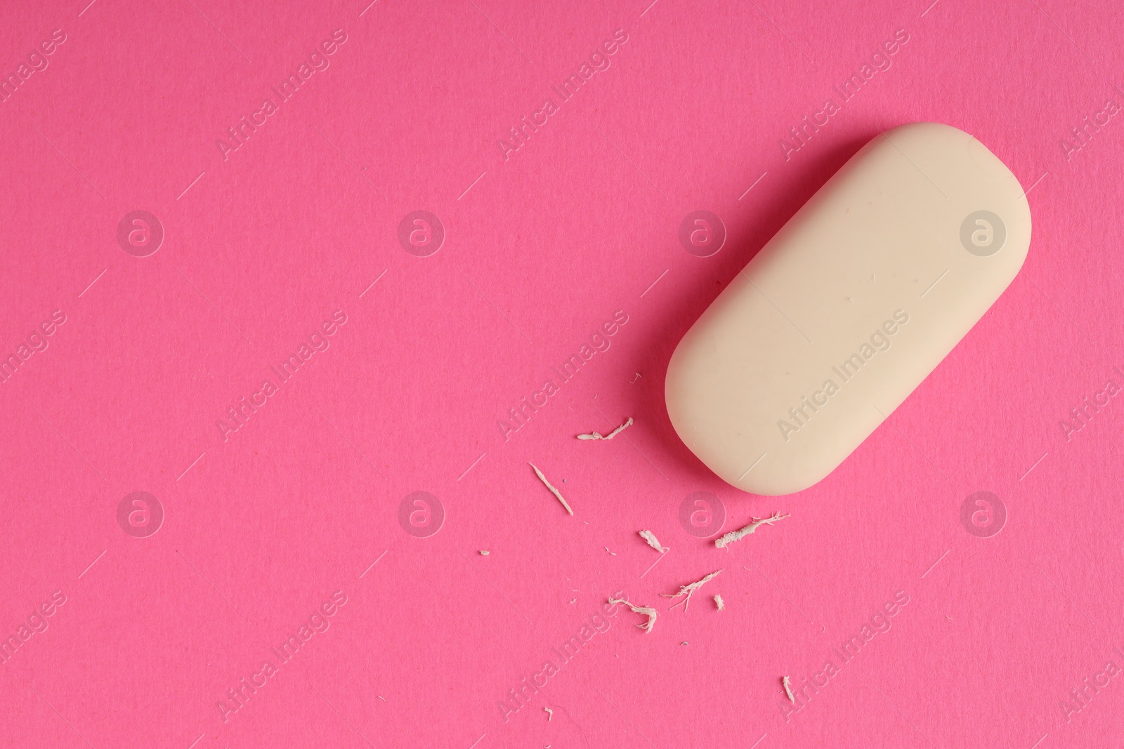 Photo of One eraser and scraps on pink background, top view. Space for text