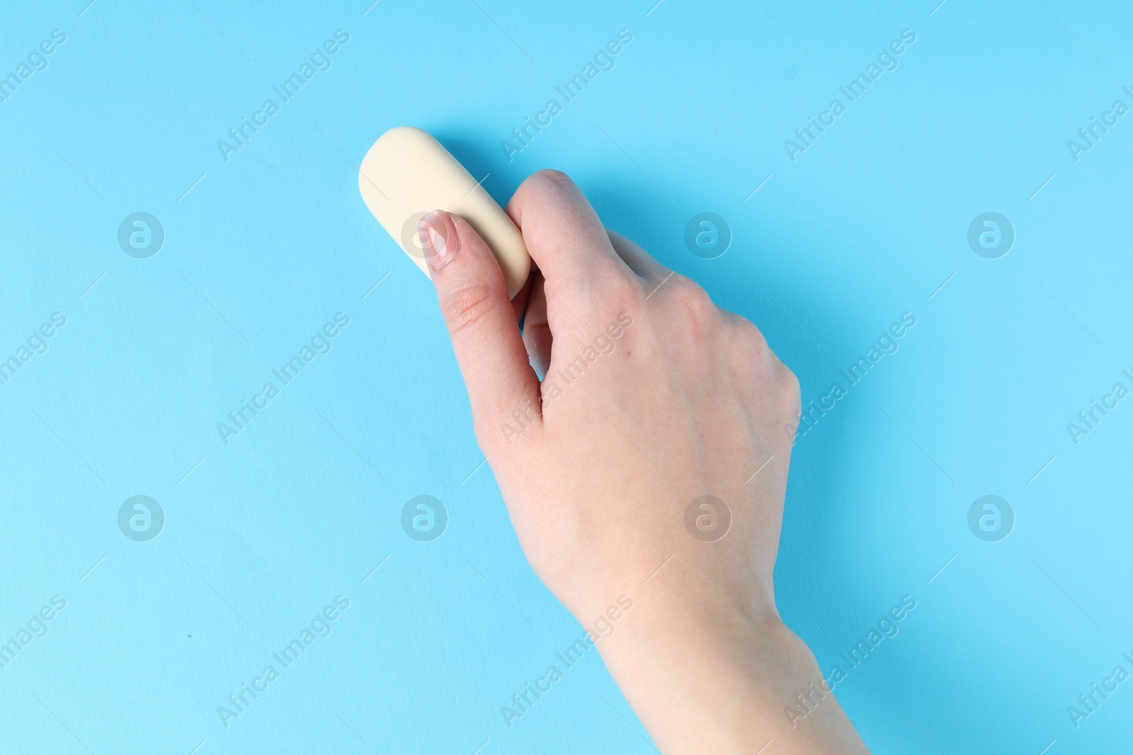 Photo of Woman using eraser on light blue background, closeup