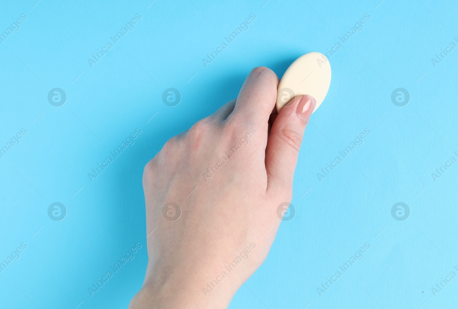 Photo of Woman using eraser on light blue background, closeup