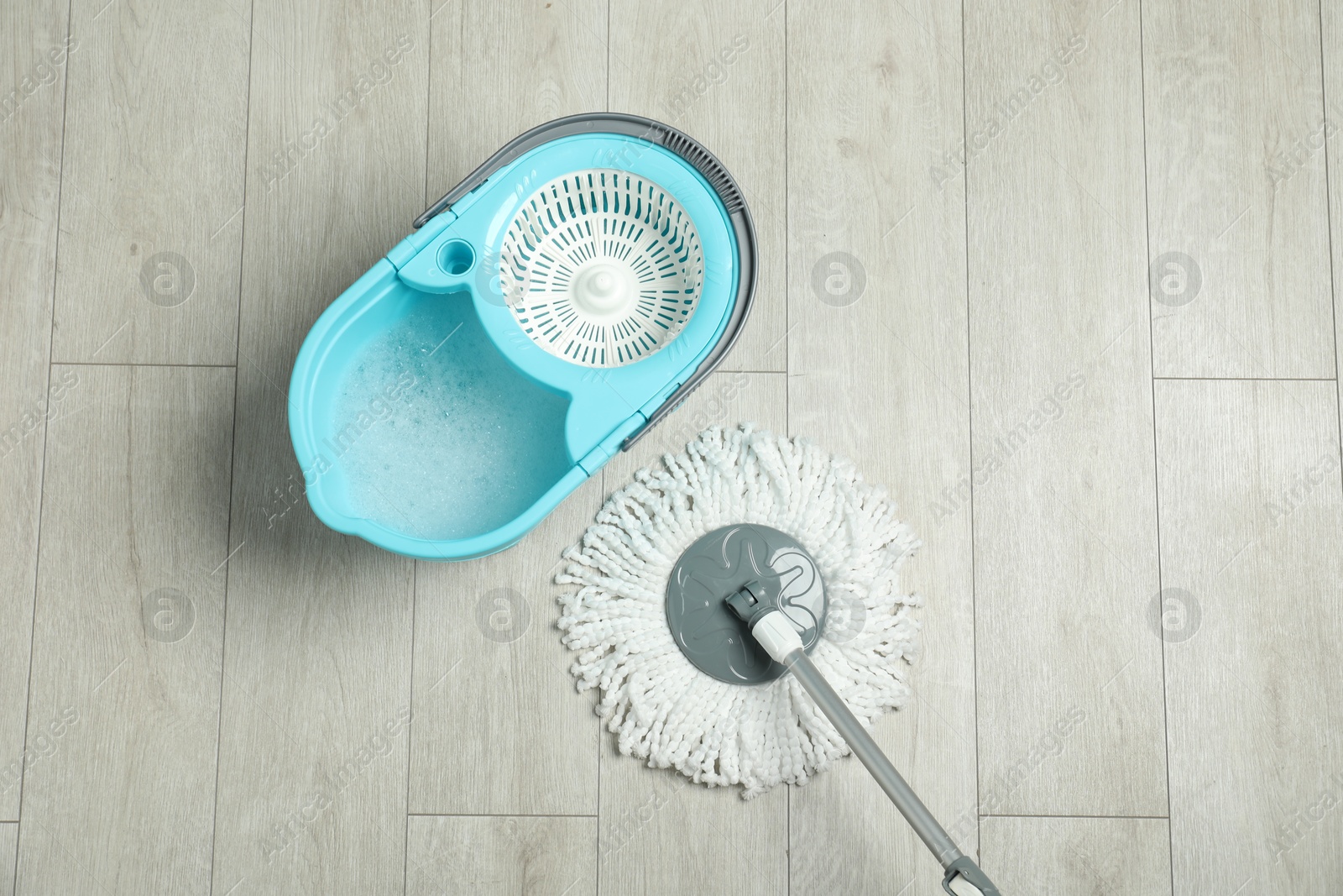 Photo of String mop and bucket with detergent on wooden floor, top view