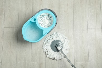 Photo of String mop and bucket with detergent on wooden floor, top view