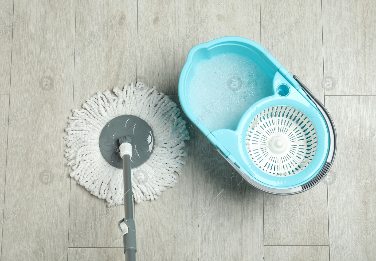 Photo of String mop and bucket with detergent on wooden floor, top view