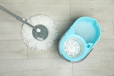 Photo of String mop and bucket with detergent on wooden floor, top view