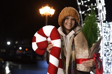 Photo of Happy woman with Christmas decor and thuja tree at night outdoors, space for text