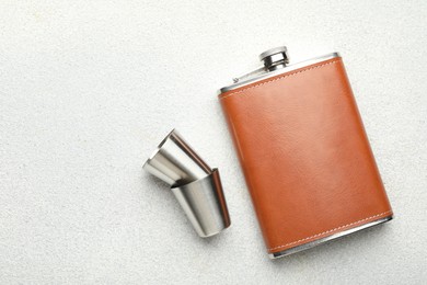 Hip flask and cups on light grey table, flat lay. Space for text