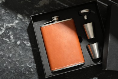 Hip flask, cups and funnel in package on dark table, top view