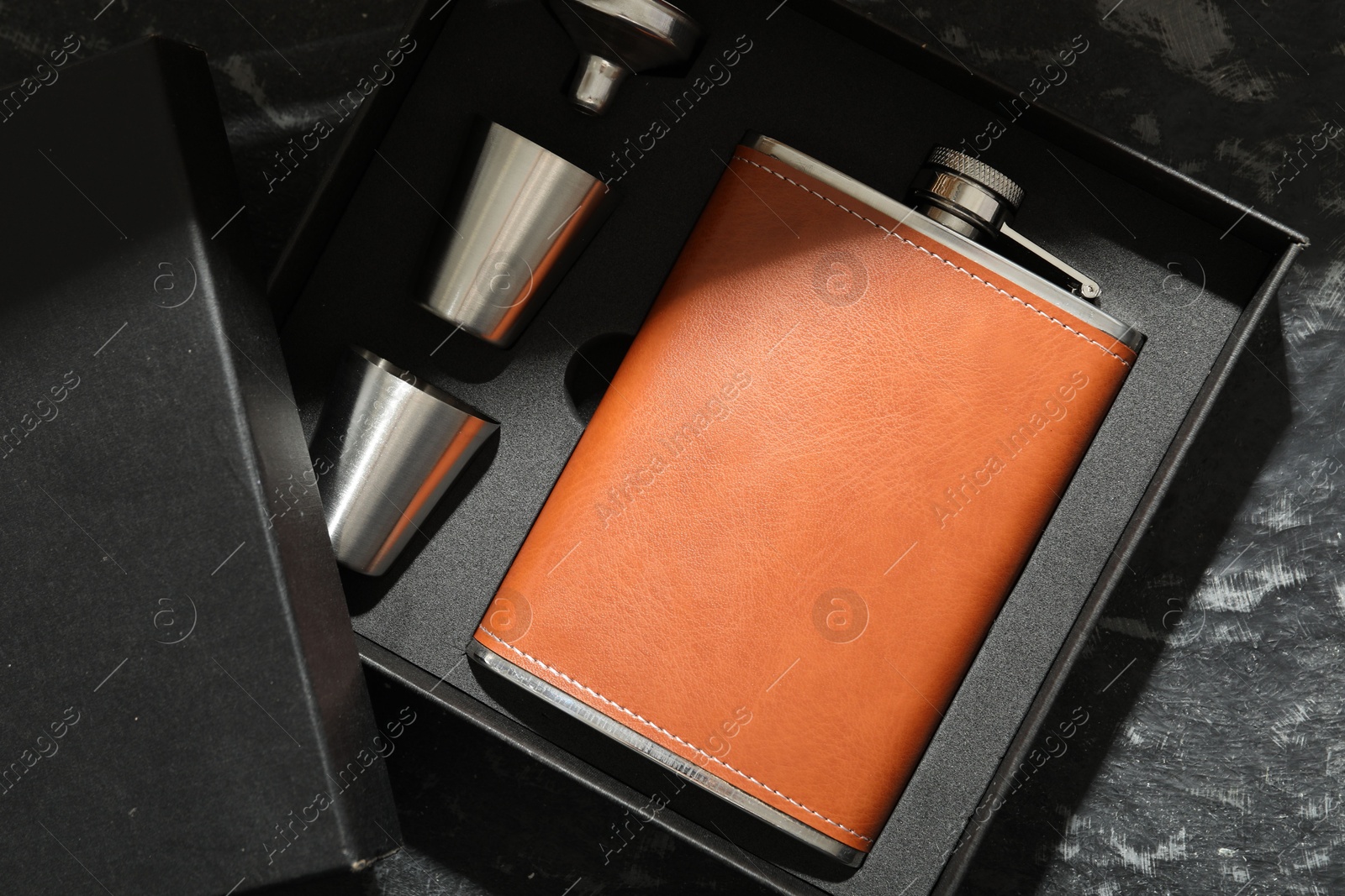 Photo of Hip flask, cups and funnel in package on dark table, top view