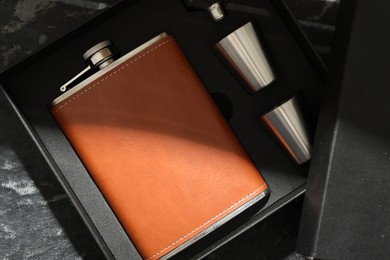 Hip flask, cups and funnel in package on dark table, top view