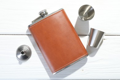 Hip flask, cups and funnel on white wooden table, flat lay