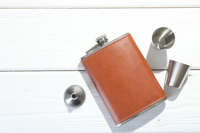 Hip flask, cups and funnel on white wooden table, flat lay. Space for text