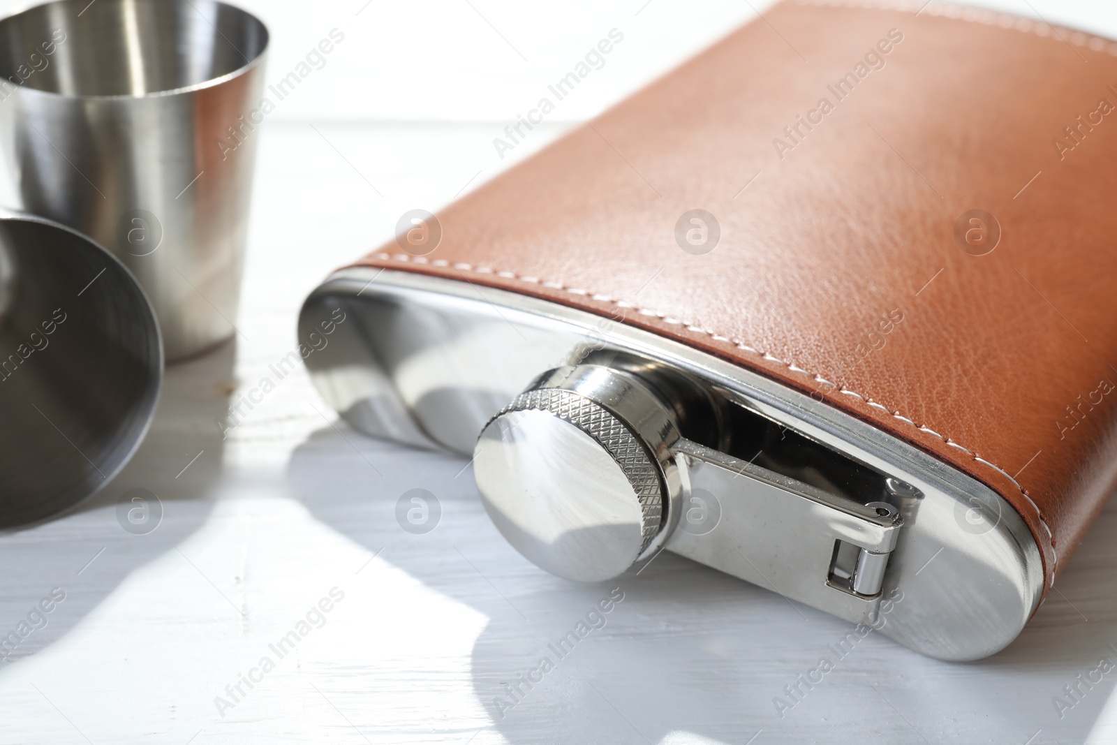 Photo of Hip flask and cups on white wooden table, closeup