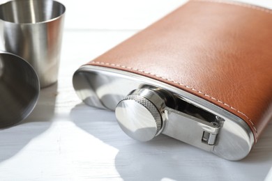 Hip flask and cups on white wooden table, closeup