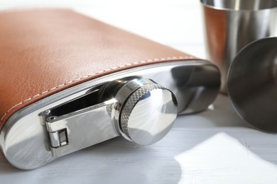 Hip flask and cups on white wooden table, closeup