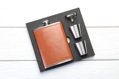 Hip flask, cups and funnel in package on white wooden table, top view