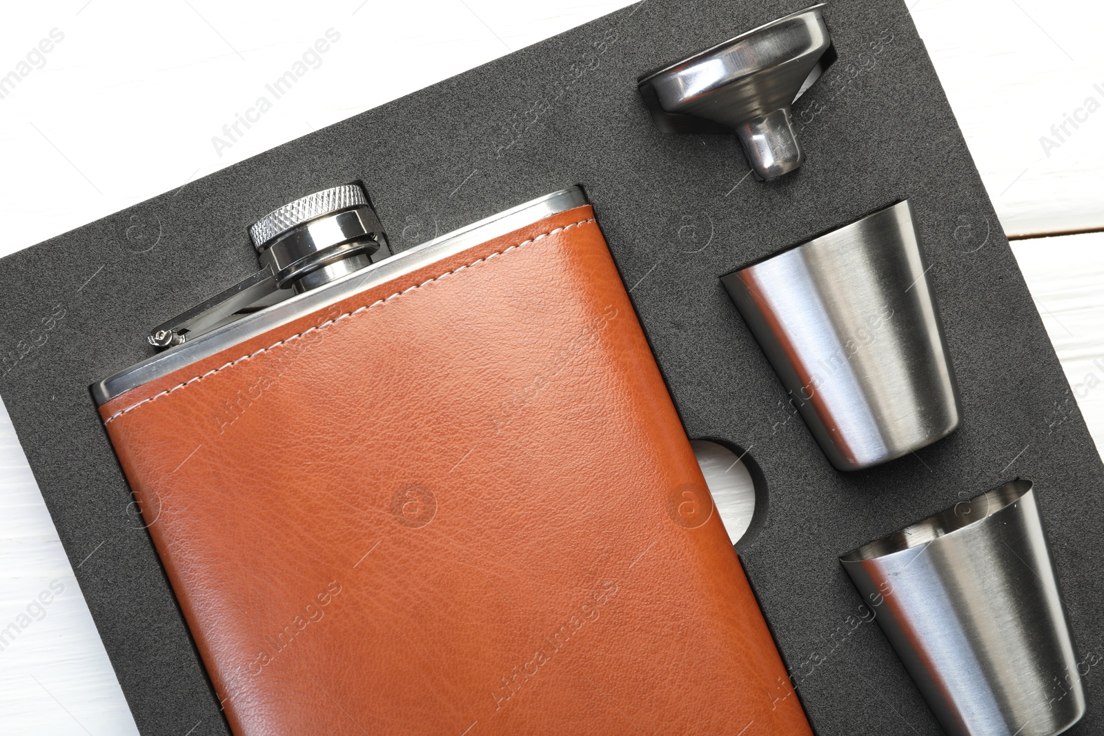 Photo of Hip flask, cups and funnel in package on white wooden table, top view