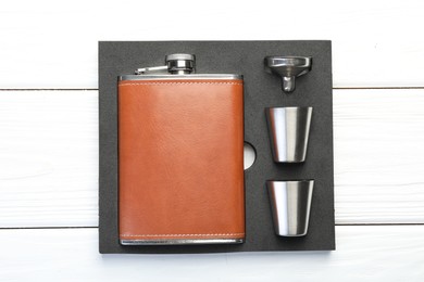 Hip flask, cups and funnel in package on white wooden table, top view