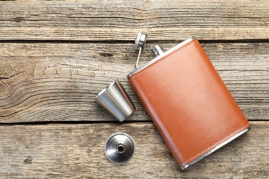 Hip flask, cup and funnel on wooden table, flat lay. Space for text