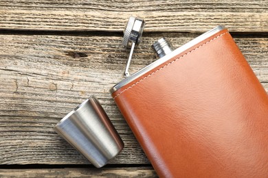 Hip flask and cup on wooden table, flat lay