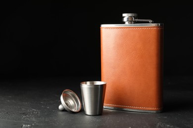 Hip flask, cup and funnel on black table, space for text