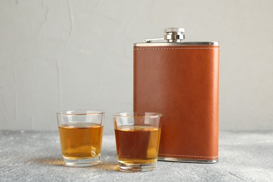 Hip flask and glasses with whiskey on grey table