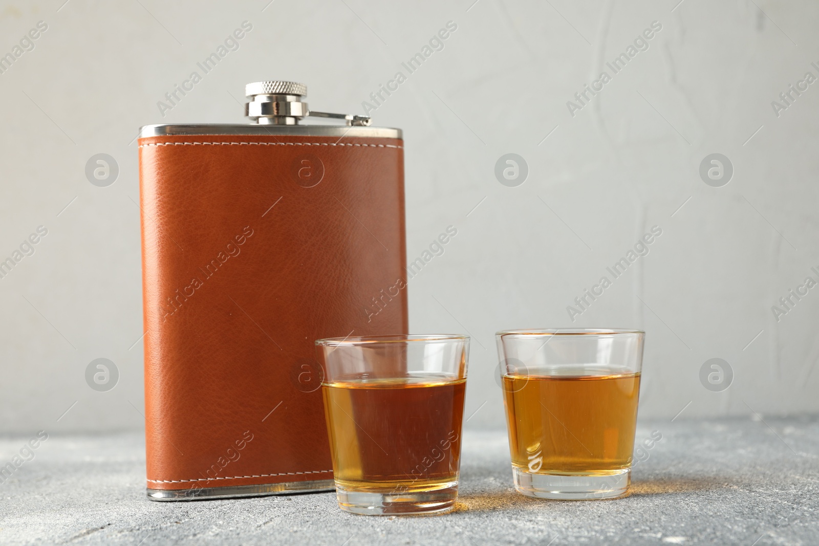 Photo of Hip flask and glasses with whiskey on grey table