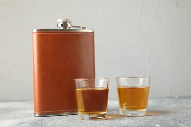 Hip flask and glasses with whiskey on grey table