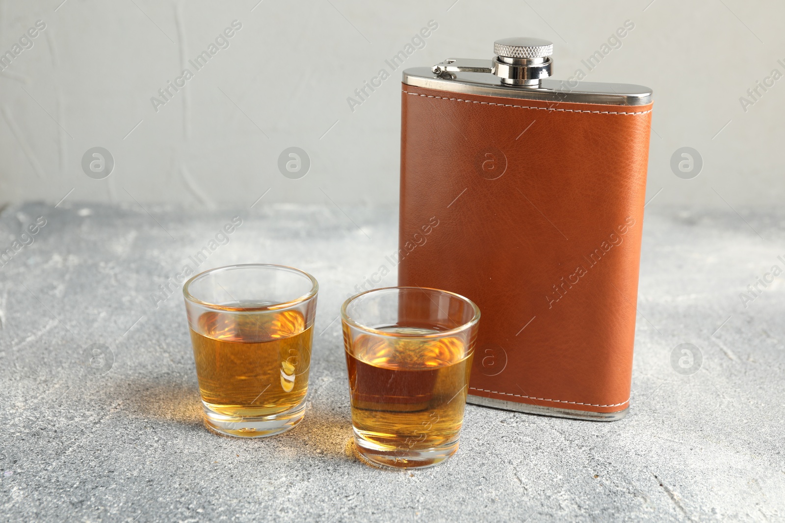 Photo of Hip flask and glasses with whiskey on grey table