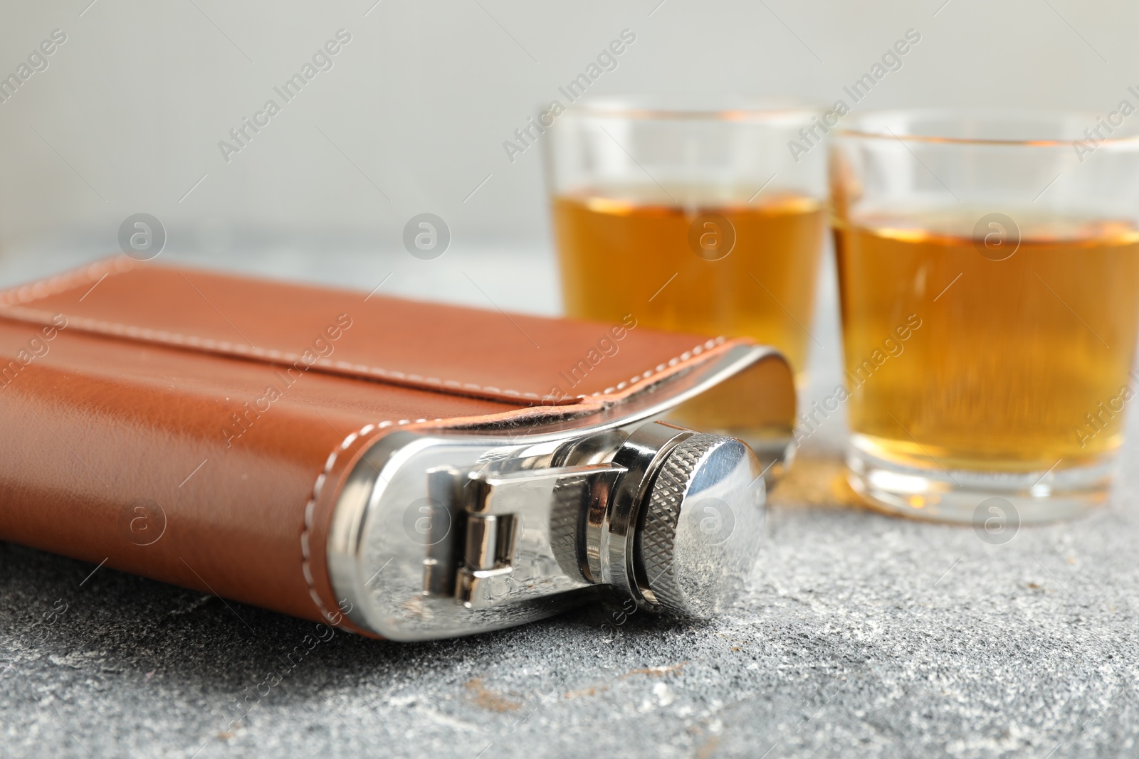 Photo of Hip flask and glasses with whiskey on grey table, closeup