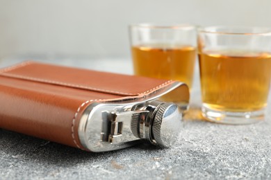 Hip flask and glasses with whiskey on grey table, closeup