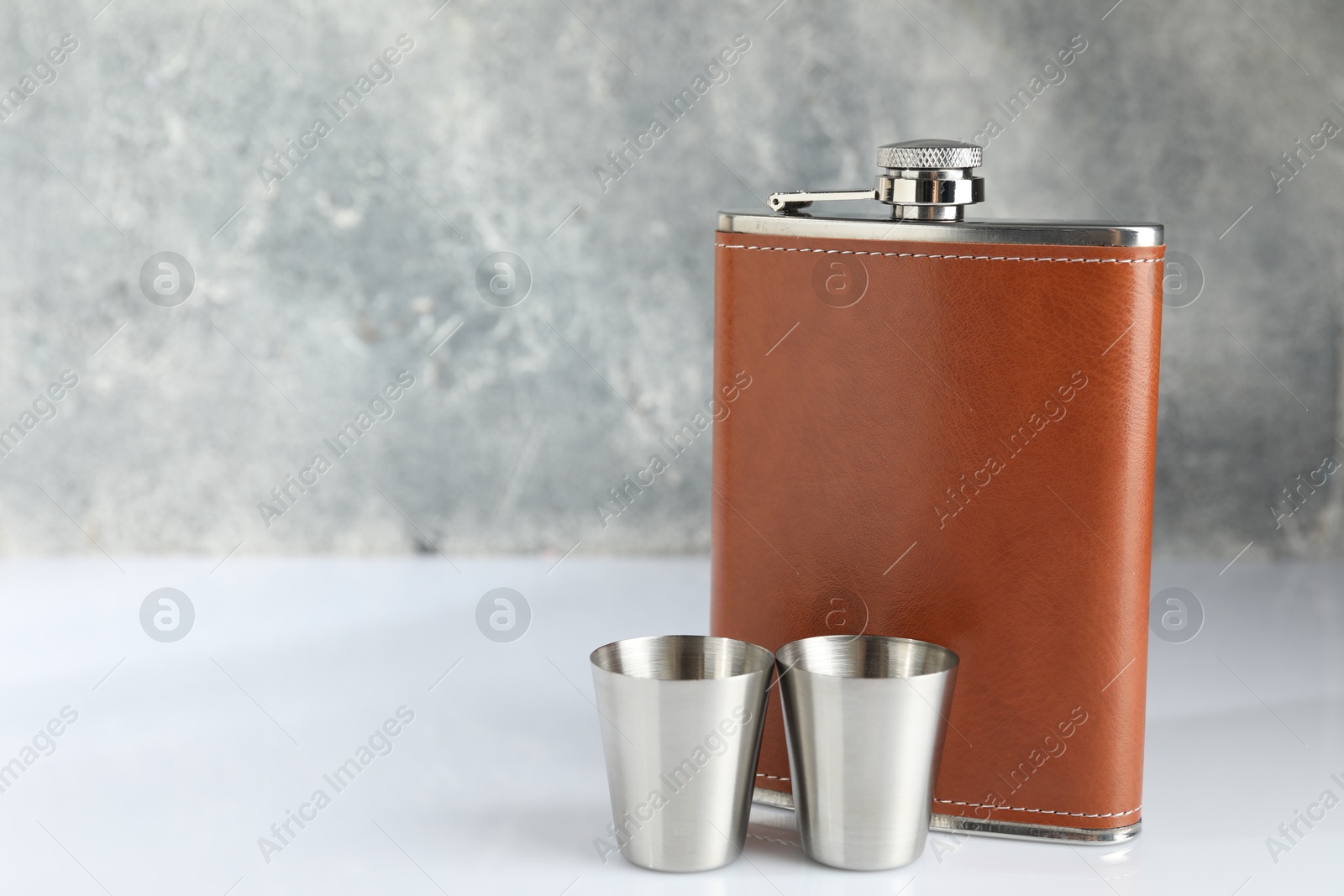 Photo of Hip flask and cups on white table. Space for text