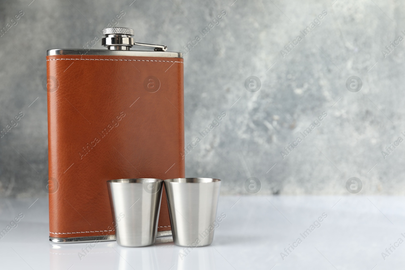 Photo of Hip flask and cups on white table. Space for text