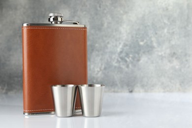 Hip flask and cups on white table. Space for text