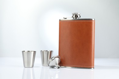 Photo of Hip flask, funnel and cups on white table. Space for text