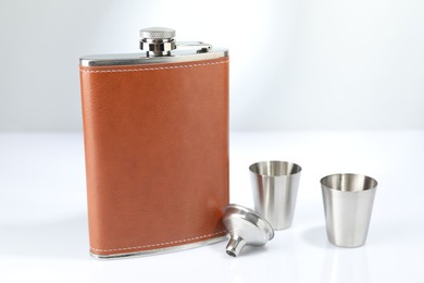 Hip flask, funnel and cups on white table