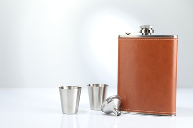 Photo of Hip flask, funnel and cups on white table. Space for text