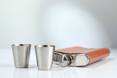 Hip flask and cups on white table. Space for text