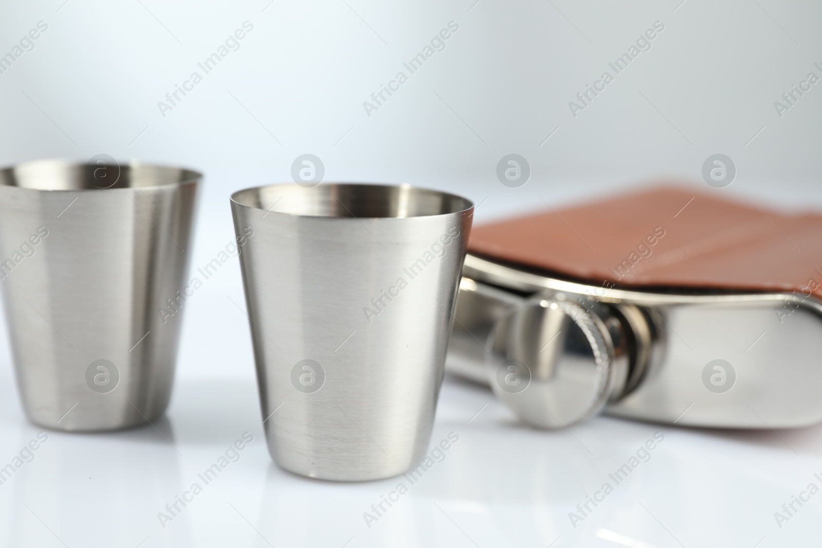 Photo of Hip flask and cups on white table, closeup