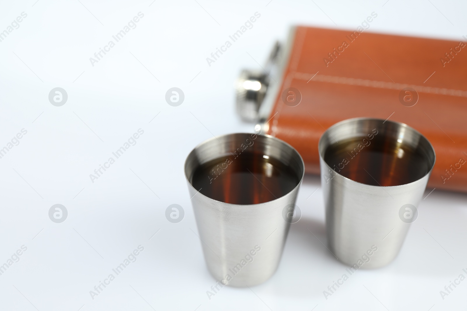 Photo of Hip flask and cups with whiskey on white table, closeup. Space for text