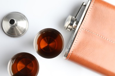 Photo of Hip flask, funnel and cups with whiskey on white table, flat lay